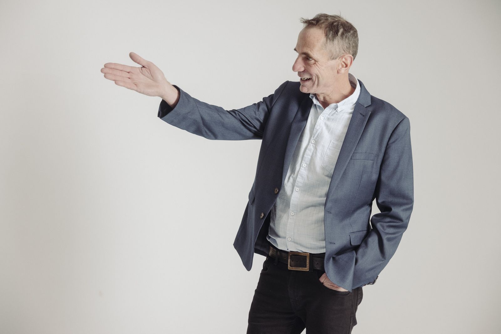 Mike Hunt in a blue blazer, smiling and gesturing welcomingly